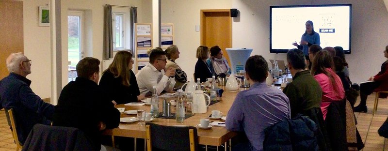 Menschen sitzen an einem Tisch und hören Vortrag