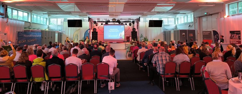 Voller Saal mit Blick auf eine Bühne